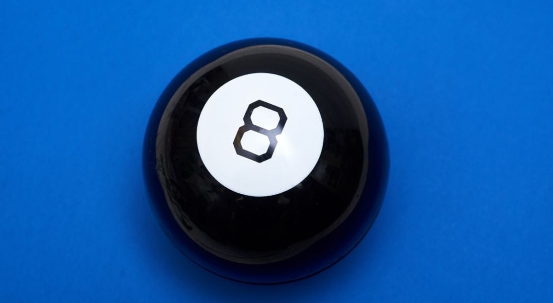 A magic 8 ball, a large black plastic sphere with the number eight, on a strong blue background.