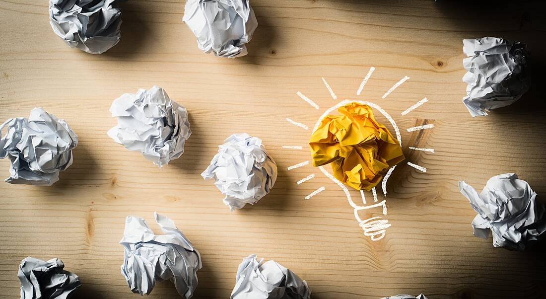 Scrunched up pieces of paper on a wooden table with one yellow and decorated like a light bulb.