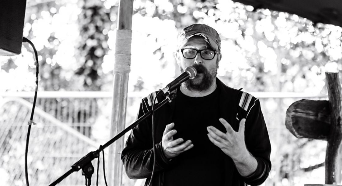 Black and white photo of Mark Graham performing his podcast live on stage.