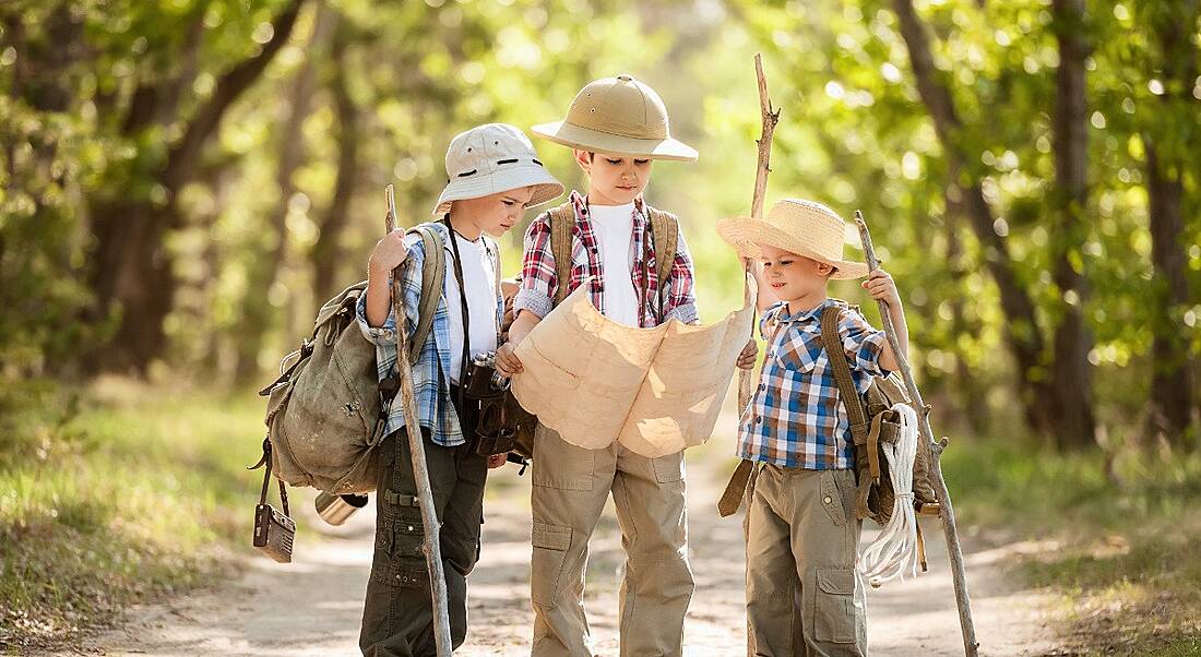 Three young boys are reading a map in adventurer clothes.