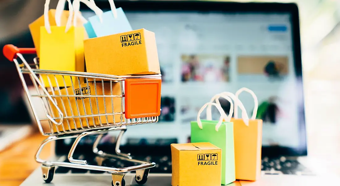 Product package boxes and shopping bag in cart with laptop, representing online retail and e-commerce.