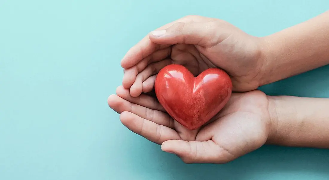 Hands holding red heart on blue background, symbolising health and wellbeing.