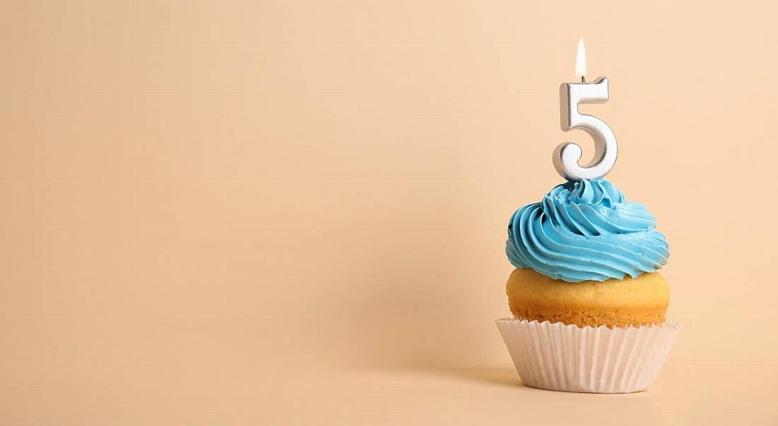 Birthday cupcake with number five candle on beige background.