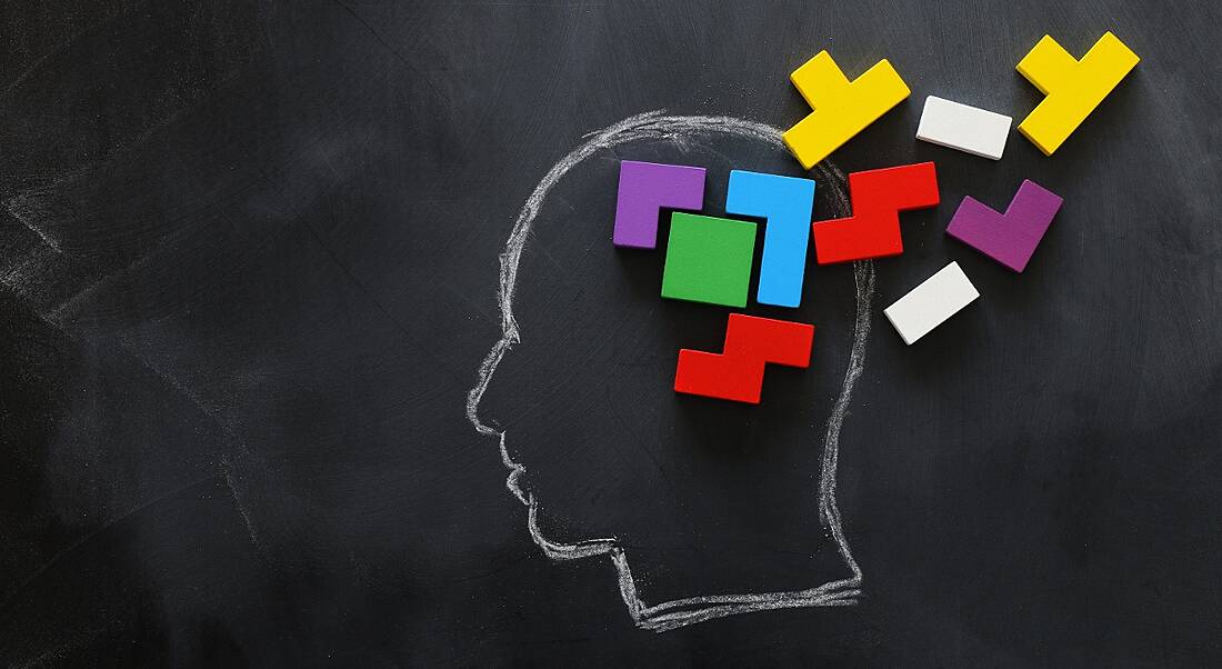 Brain made from colourful wooden puzzle inside chalk drawing of a human head on a blackboard.