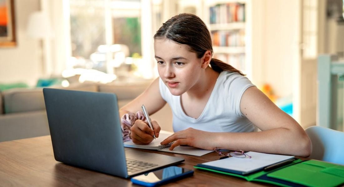 Teenage girl studying online at home looking at a laptop.