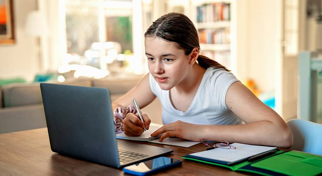 Teenage girl studying online at home looking at a laptop.