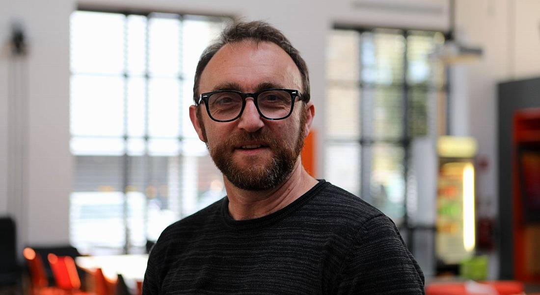 Owen Murray of Zalando Dublin is standing in a brightly lit office and smiling into the camera.