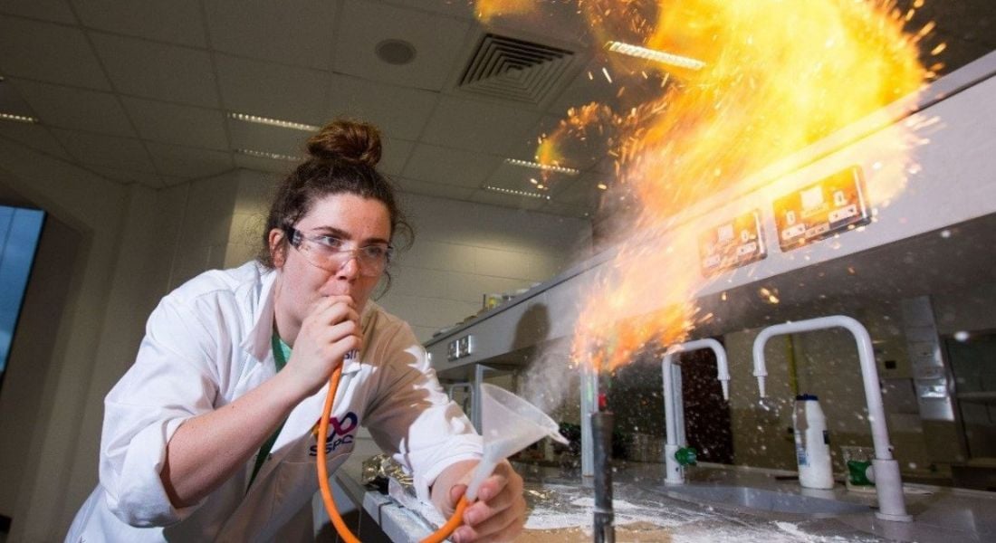 Laurie Ryan is in a lab blowing flames from a funnel.