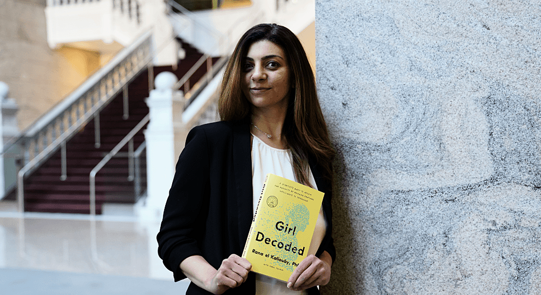 Rana el Kaliouby of Affectiva is standing in a brightly lit space and holding a copy of her book, Girl Decoded.