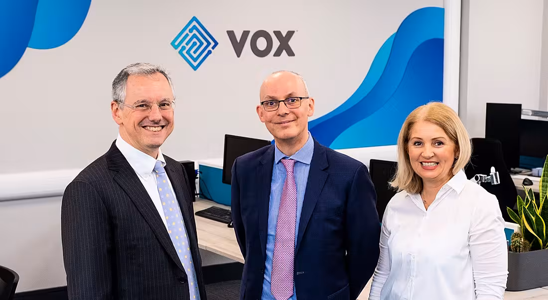 Three business people are standing together and smiling into the camera at the Vox Financial offices.