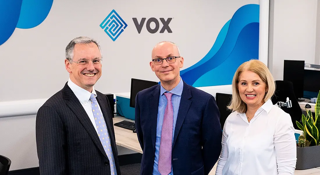 Three business people are standing together and smiling into the camera at the Vox Financial offices.