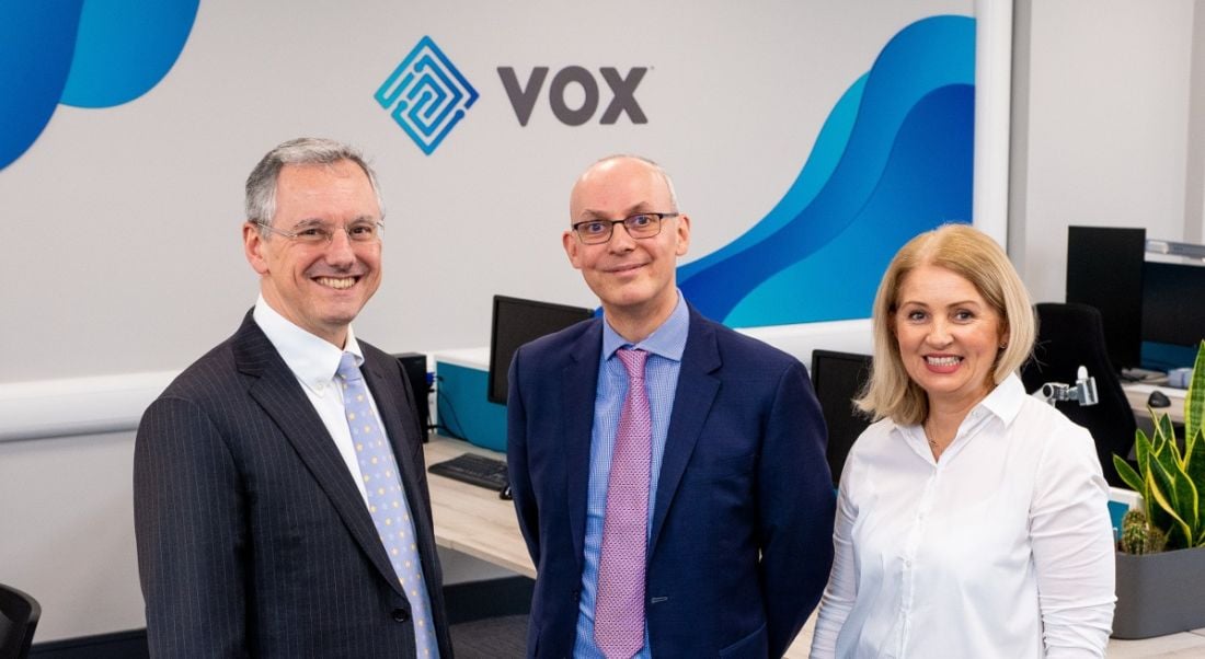 Three business people are standing together and smiling into the camera at the Vox Financial offices.