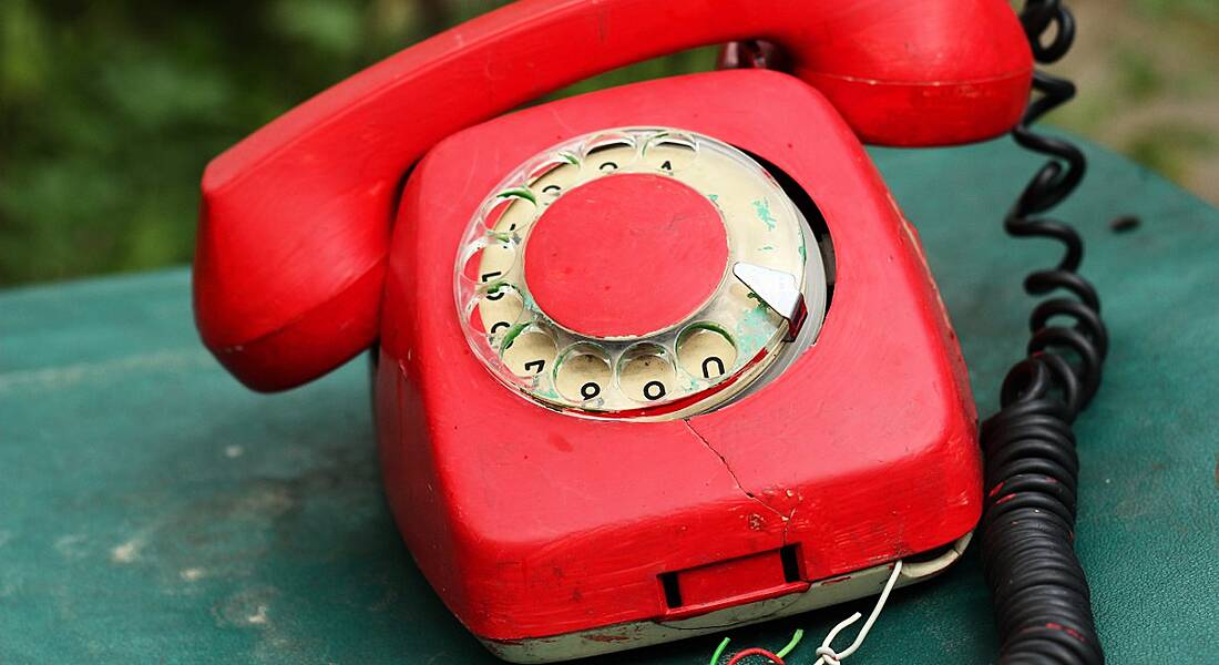 A broken red rotary telephone on a rusty green surface.