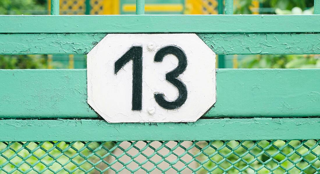 Number 13 sign on a teal metal fence.