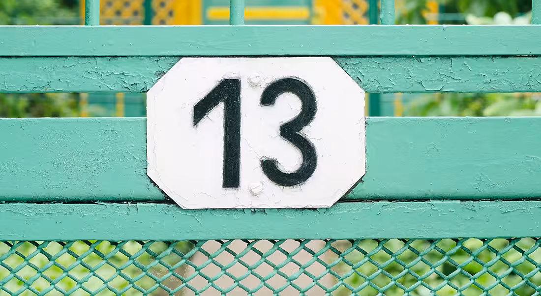 Number 13 sign on a teal metal fence.