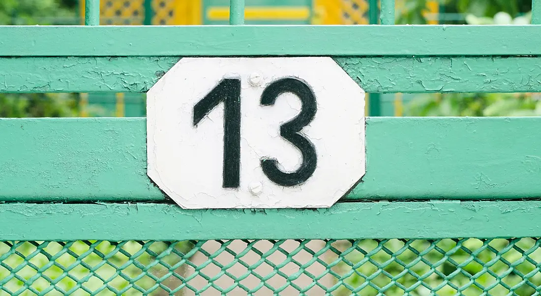 Number 13 sign on a teal metal fence.