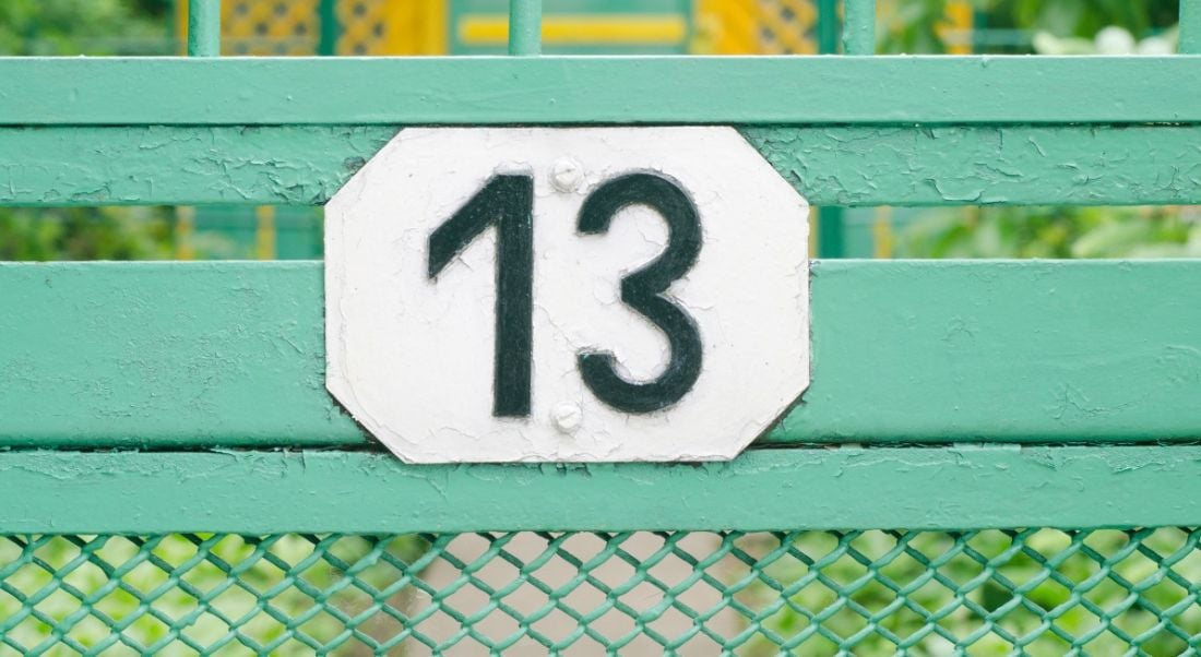 Number 13 sign on a teal metal fence.