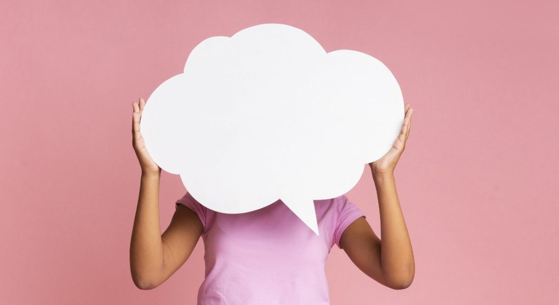 A person in a pink T-shirt is holding up a white thought bubble against a pink background.