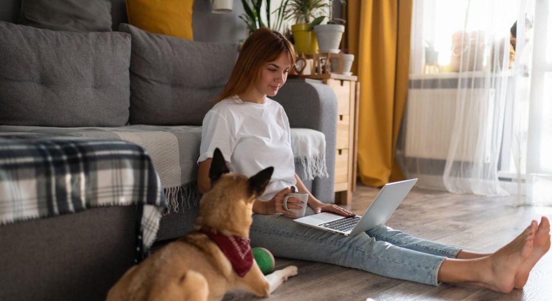 A woman is working in her home as her dog sits beside her.