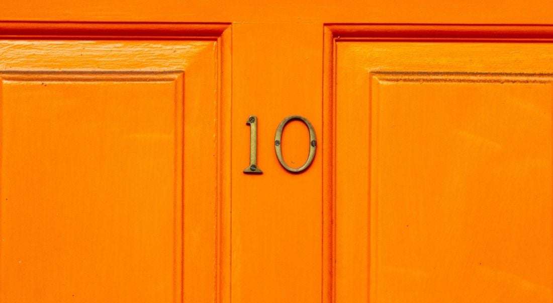 A bright orange front door with a gold number 10 nailed to it.