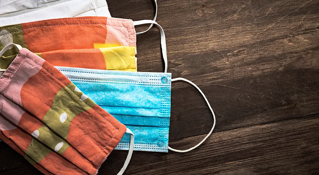 Colourful face coverings are lying on a dark wooden table.