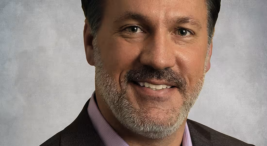 Chris Huff of Kofax is smiling into the camera in front of a grey background.