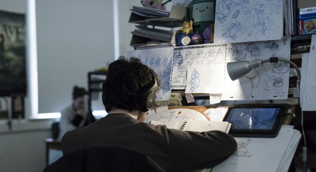 An animation student is working at a station in IADT, surrounded by sketches.