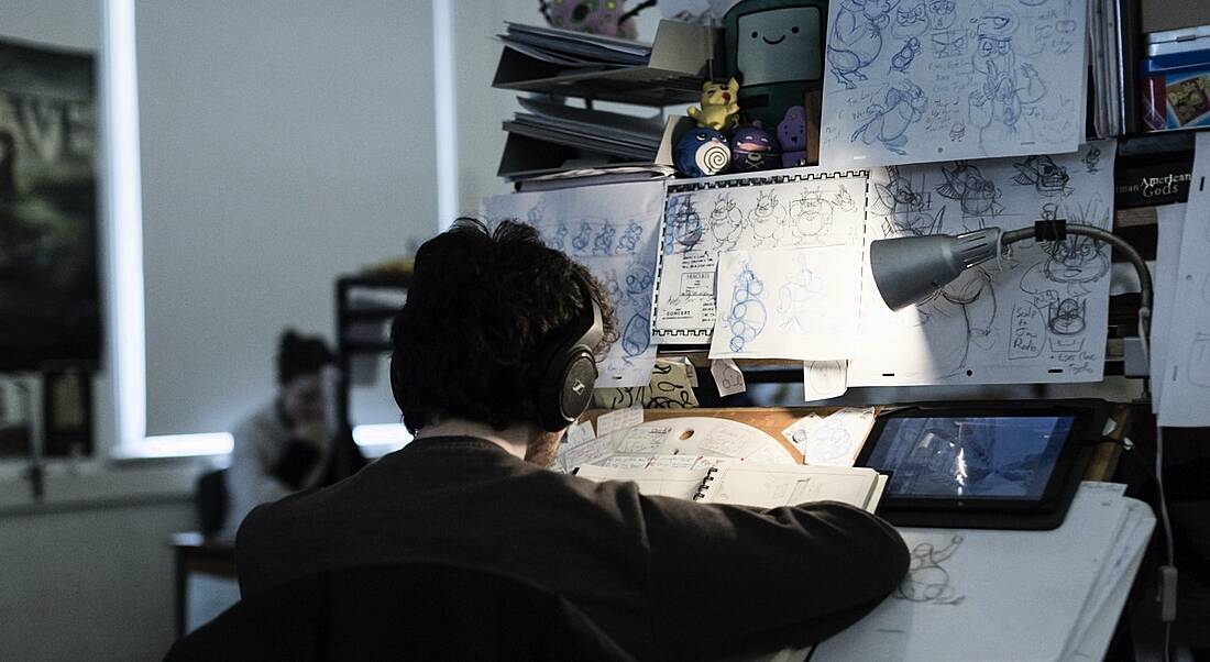 An animation student is working at a station in IADT, surrounded by sketches.