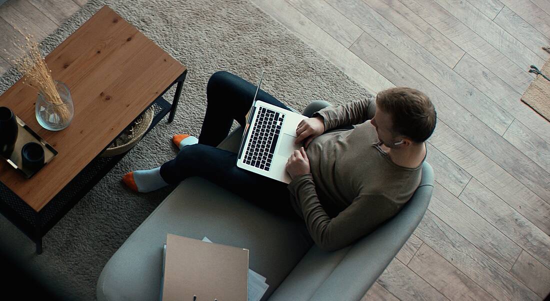 An aerial view of a man remote-working on a laptop on his couch.