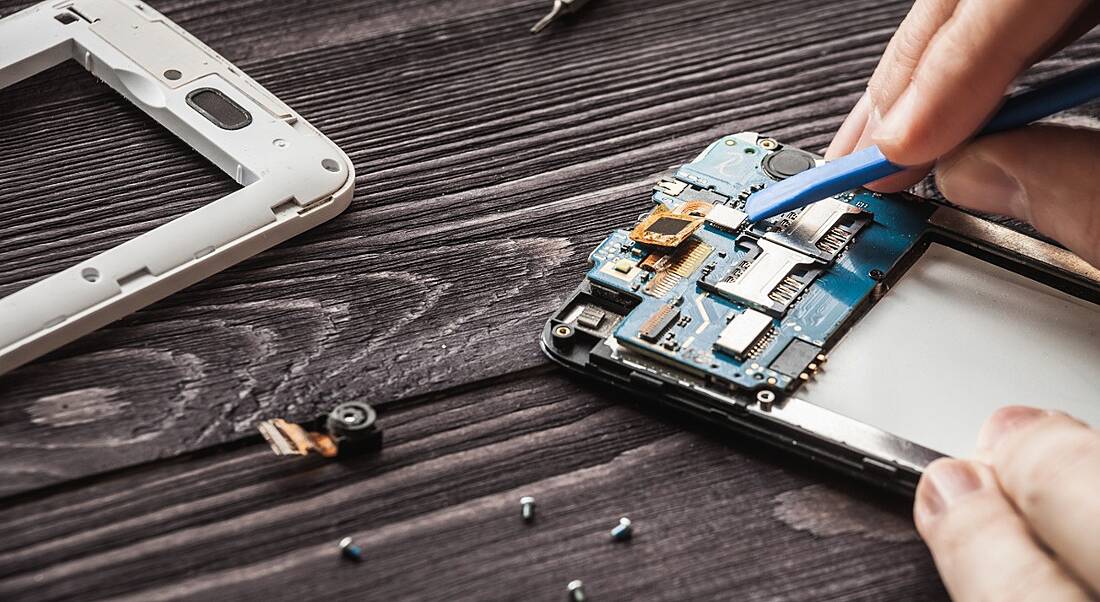 A mobile device is being repaired on a wooden table.