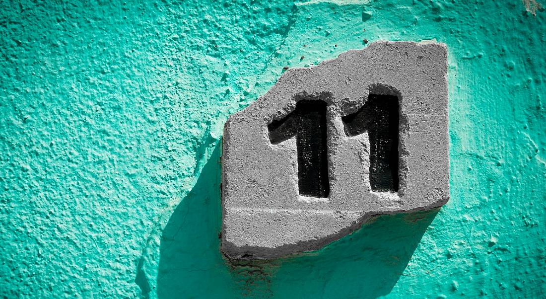 The number eleven engraved on a stone, which is placed against a teal stone wall.