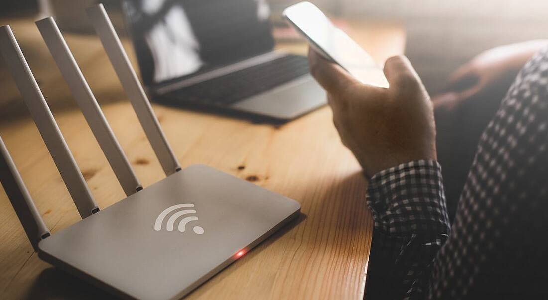 Close-up of a wireless router and a person using a smartphone at home.