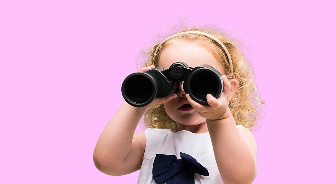 A small child is looking through binoculars on a pink background.