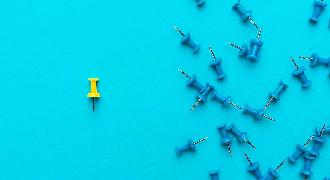 A yellow pin separated from a group of blue pins on a blue background, symbolising isolation.