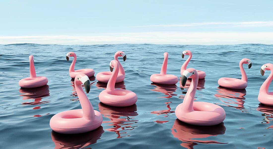 Inflatable flamingos are bobbing on the water's surface in the ocean.