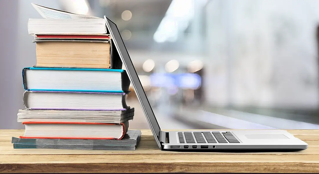 Stack of books with laptop on wooden table for training and development.