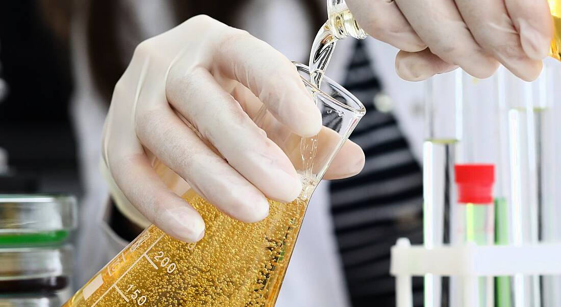 Close-up of a person's hands pouring chemicals in a lab.