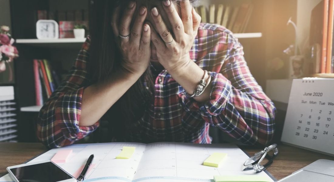 A woman is sitting at a desk with her heads in her hands, surrounded by work.