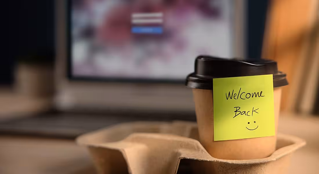 A cup of coffee is sitting on an office desk welcoming an employee back to work.