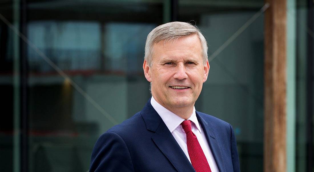 Alastair Blair of Accenture is wearing a suit and red tie and standing outside while smiling into the camera.