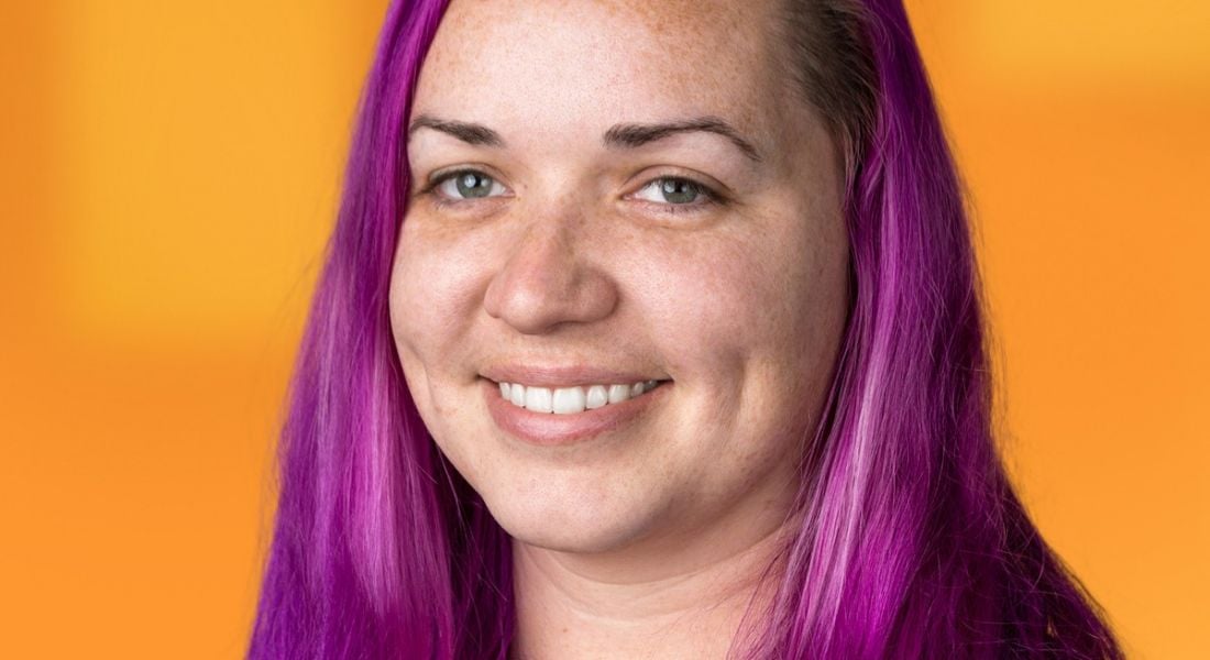 Chrystal Taylor, a head geek at SolarWinds, is smiling into the camera against a bright orange background.
