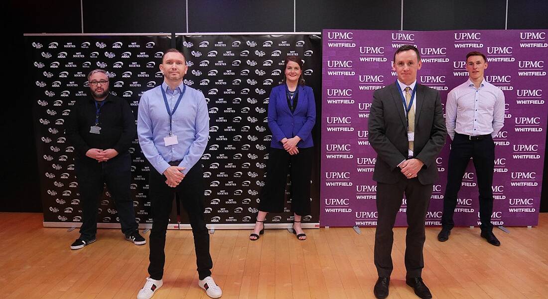 The team behind the new e-sports scholarship at Waterford IT is standing in a sports hall and smiling into the camera.