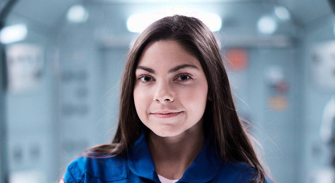 Alyssa Carson is standing in an astronaut uniform and smiling into the camera.