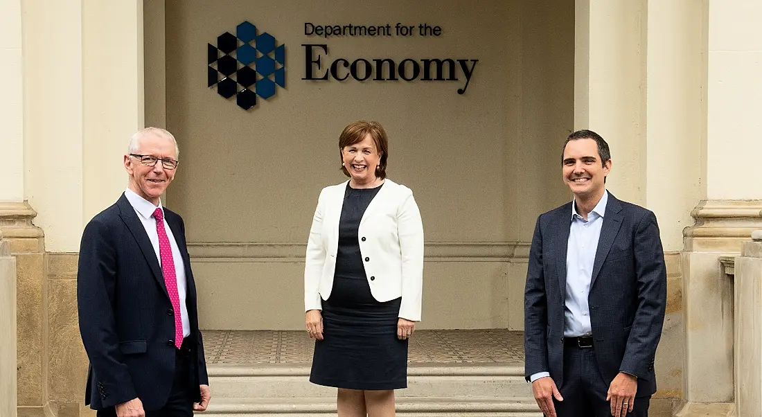 Two men and a woman in business attire stand outside the Department of the Economy in Northern Ireland.