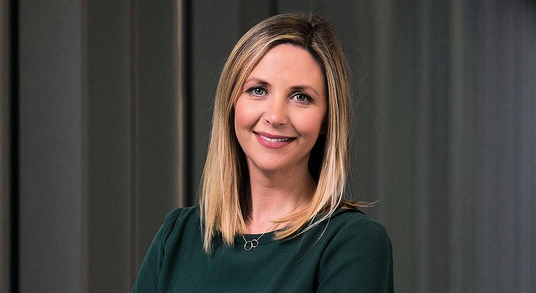 Audrey O’Mahony of Accenture is standing in front of a grey curtain and smiling into the camera.