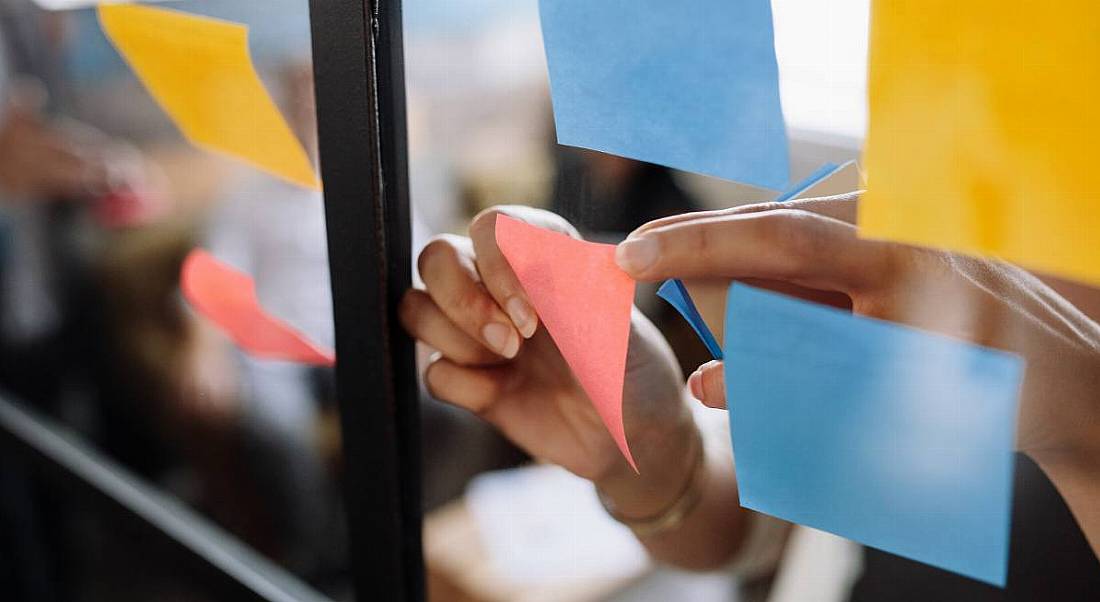 Close-up shot of hands sticking notes on glass wall in an office.