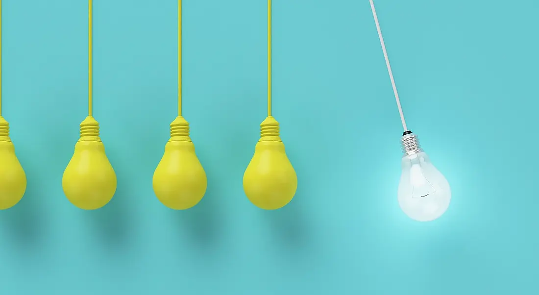 Five yellow lightbulbs hanging against a blue background, with one white lightbulb shining brightly beside them.