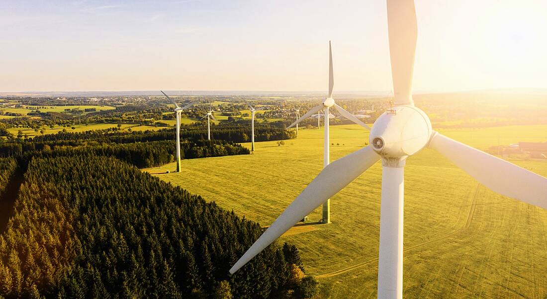 Wind turbines across a green field below a bright blue sky.