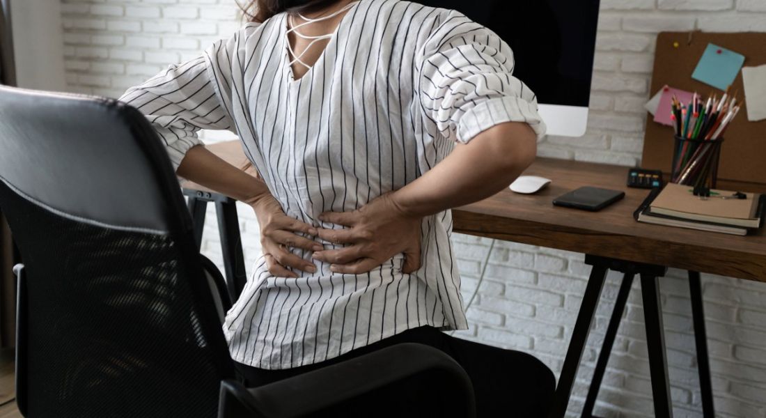 A woman is suffering from back pain in her home office.