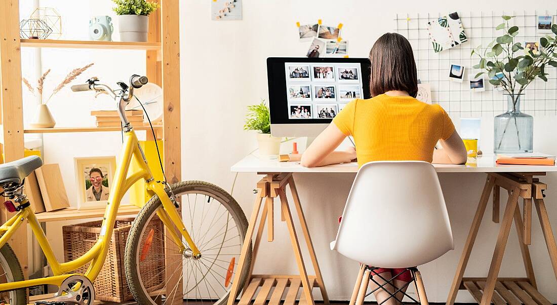 A woman is wearing a yellow top and sitting at her desk doing work, symbolising presenteeism.